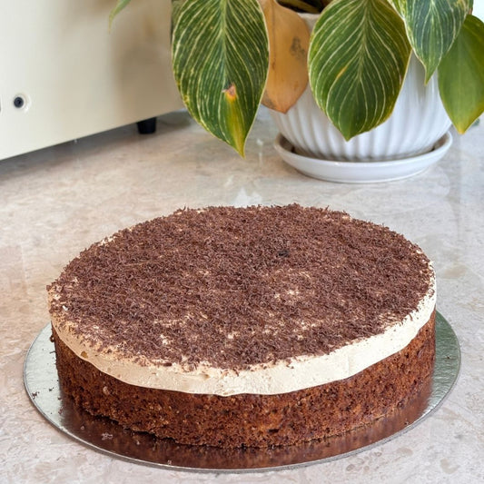 Chocolate cake with cream filling on a metal tray, with a plant in the background.