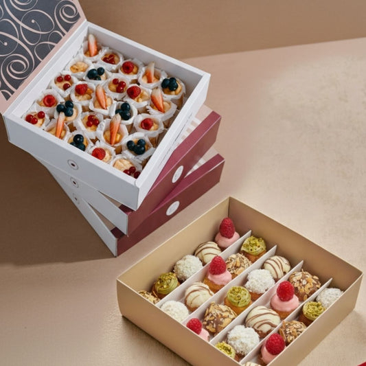 Two boxes of assorted small desserts on a beige surface