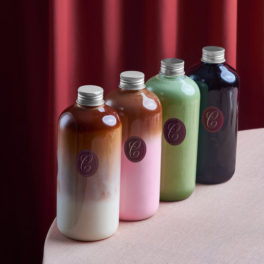 Four bottles of different colors with silver caps on a red curtain background